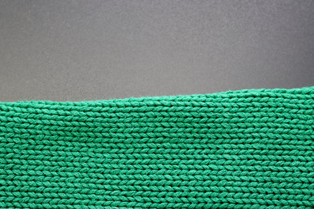 The texture of a dense knitted sweater of emerald color on a gray background. Texture, background,...