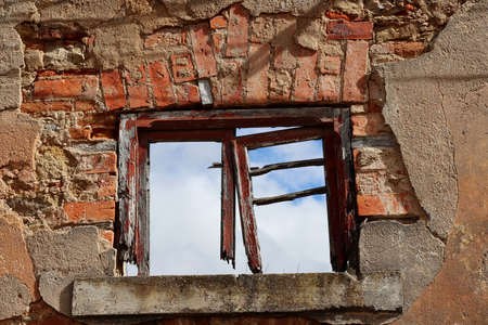 Old window without glass and with a broken wooden frame on a brick wallの写真素材