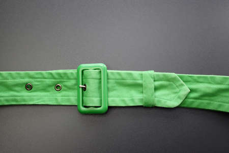 Women's green fabric belt with a plastic buckle and metal tongue and holes. Green belt on a gray background.の写真素材