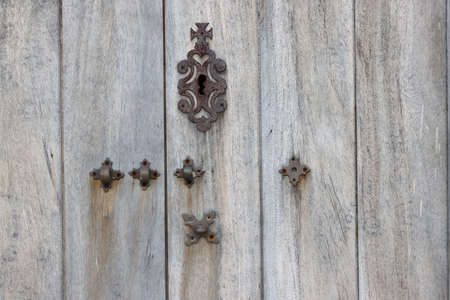 Rusty metal keyhole cover plate and metal hinges padlock on the old wooden door.の写真素材