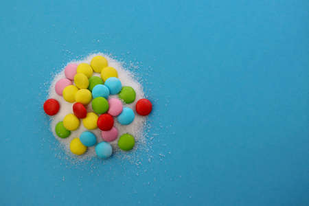 Multi-colored sweet dragees are immersed in white sugar. Sweets and sugar on a blue background.の写真素材