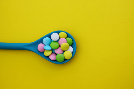 Multicolored sweet drops in a blue spoon on a yellow background.の写真素材