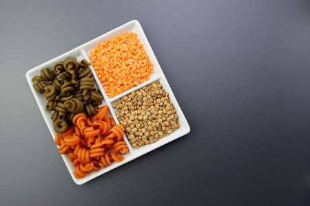 Green and red trotolle pasta, green and red lentils in a square plate. Colored pasta and lentils on a gray background.の写真素材