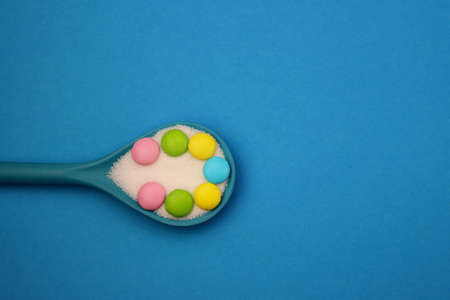 Multicolored sweet drops and white sugar in a blue spoon on a blue backgroundの写真素材