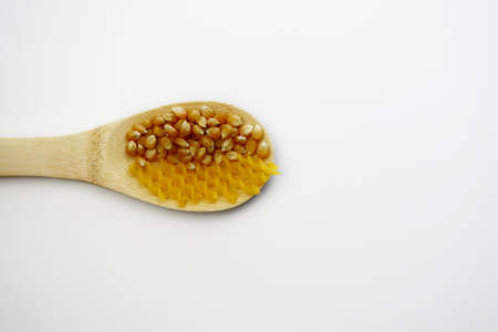 Yellow fusilli pasta and corn grains in a wooden spoon on a white background. Fusilli pasta made from cornmeal.の写真素材