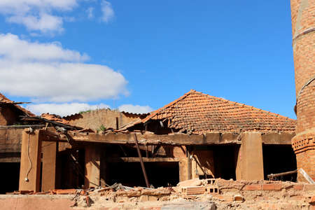 Brick building after fire with destroyed tiled roof against blue sky. broken and destroyed roof of an old abandoned industryの写真素材