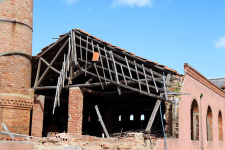 Brick building after fire with destroyed tiled roof against blue sky. Broken roof and rafters.の写真素材