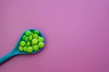 Green sweet drops in a blue spoon on a light pink backgroundの写真素材