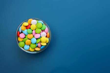 Multicolored sweet candies in a round bowl on a blue background.の写真素材