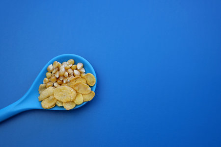 Cornflakes and corn grains in a blue spoon on a blue background.