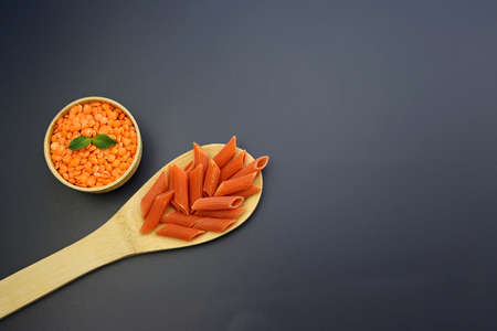 Red penne pasta in a wooden spoon and red lentils in a round bowl on a gray background. Red Lentil Penne Paste.の写真素材
