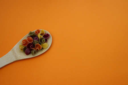 Multi-colored pasta margarita in a wooden spoon on an orange background.の写真素材