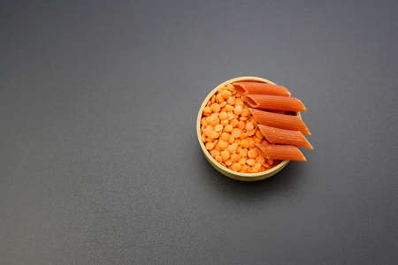 Red lentils and red penne pasta in a round bowl on a gray background.の写真素材