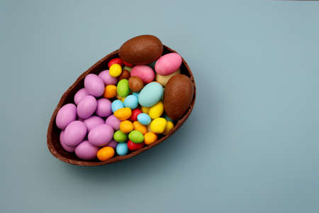 Multicolored sweet dragees in the form of an egg in a chocolate bowl on a blue background. Chocolate eggs.の写真素材