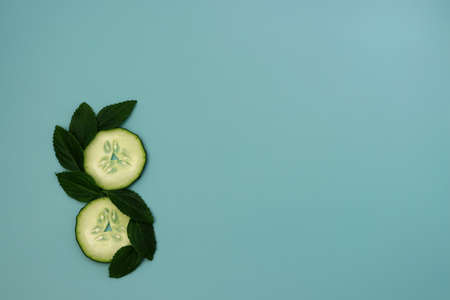 Cucumber circles and green mint leaves are laid out in the shape of the number eight. Cucumbers on a blue background.の写真素材