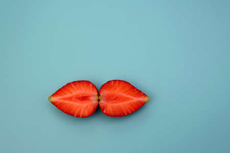 Juicy fresh strawberries, split into two halves on a blue background.の写真素材