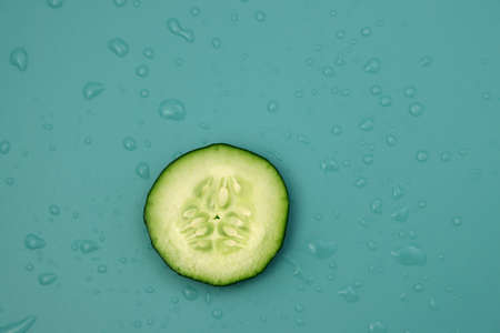 A small circle of fresh cucumber on a blue background with water drops. Low-calorie and watery vegetable.の写真素材