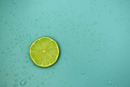Slice of fresh lime on a blue background with water drops. Citrus background.