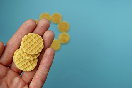 Small round waffles in a female hand on a blue background.