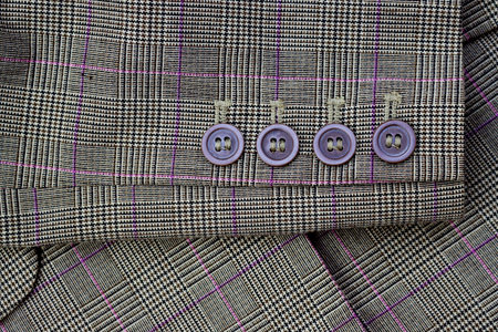 Brown buttons on the sleeve of a women's plaid jacket. Checkered fabric texture with buttons.