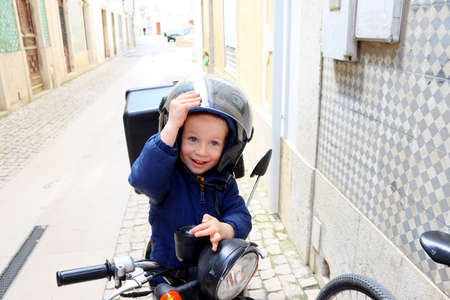 Portrait of a happy little boy in a motorcycle helmet. A joyful child sits on a motorcycle and opens the visor on his helmet.の写真素材