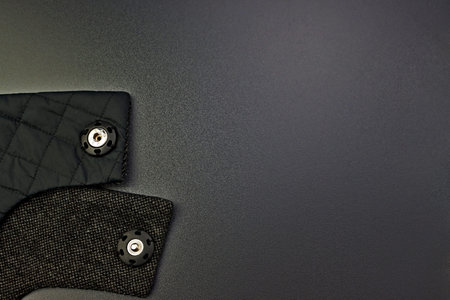 Close-up of woolen fabric with rivets on a dark gray background. Accessories for outerwear. Part of...