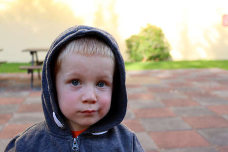 Portrait of a pensive boy in a hood. A three-year-old blond boy with a sad look.の写真素材