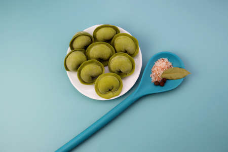 Green frozen dumplings in a round plate and a blue spoon with spices. Homemade frozen dumplings on a blue background.の写真素材