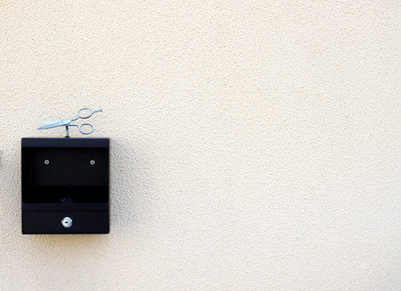 Modern cigarette metallic ashtray at the entrance to the hairdresser. A black ashtray with scissors hangs on a yellow wall. Outdoor smoking area zone.の写真素材