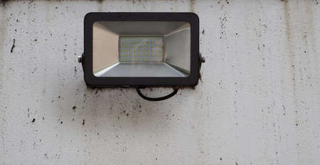 A rectangular LED lamp hangs on a dirty white wall. Street lighting.の写真素材
