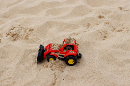 Red plastic bulldozer in the sand. Toy construction equipment. Children's toys on the beach.の写真素材