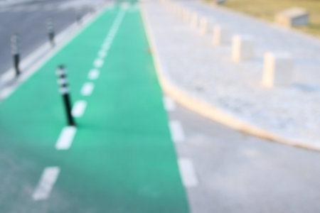 Blurred background of a city street divided into a green cycle path and a pedestrian zone.