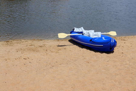 Blue rubber boat and oars on the sandy bank of the river. inflatable boat, side view.の写真素材