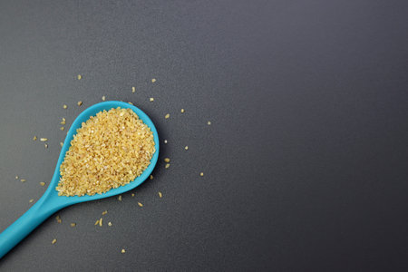 Dry bulgur wheat grains in a blue spoon on a gray background. bulgur a staple of Middle Eastern cookingの写真素材