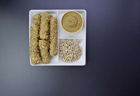 Breadsticks, peeled sunflower seeds and sunflower seed paste in a square plate on a gray background.の写真素材