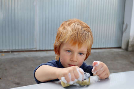 The blond boy stares intently at the soapy sponge. A four-year-old boy squeezes a sponge tightly in his hand.の写真素材
