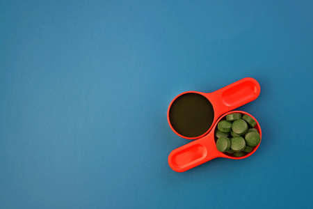Spirulina powder and tablets. Spirulina in red measuring spoons on a blue background.の写真素材