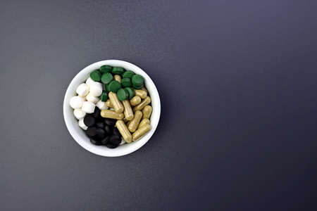 Four types of dietary supplements in tablets. Food supplements in a round white bowl on a gray background.の写真素材