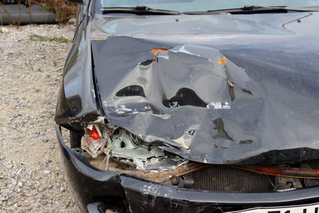 Front view close up of a crashed car. Broken headlight and dent on the hood of a black car. Car after an accident.の写真素材
