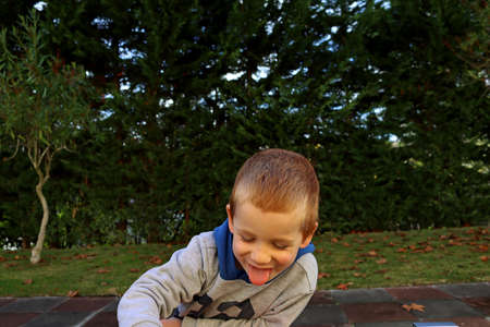 The blond boy put his head down and sticks out his tongue. A four-year-old boy is teasing and laughs.の写真素材