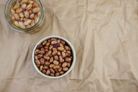 Dry beans in a round bowl and beans soaked in water on a background of crumpled paper. brown beans