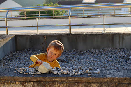 The blond boy is playing with stones. A five-year-old boy sits among the stones and carefully arranges them.の写真素材