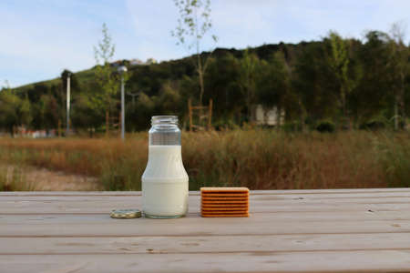 Milk in a glass bottle and a stack of cookies on a wooden table on a blurred green background.の写真素材