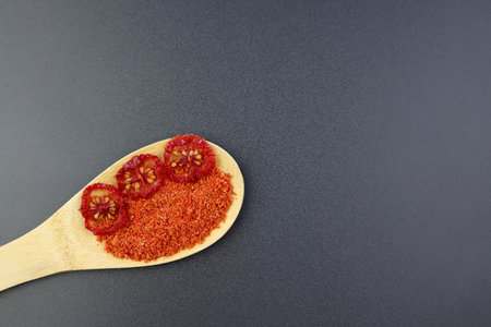 Dried tomatoes and tomato powder in a wooden spoon on a gray background. Crushed sun-dried tomatoes.