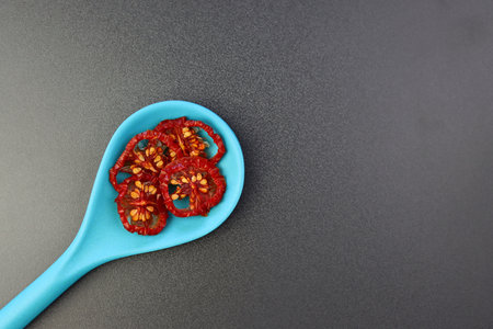 Dried tomato slices in a blue spoon on a gray background.の写真素材