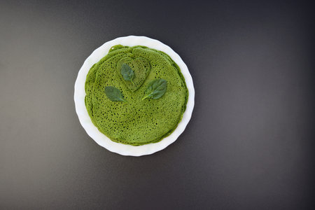 Delicious green spinach crepes on white round plate, gray background, top view.の写真素材