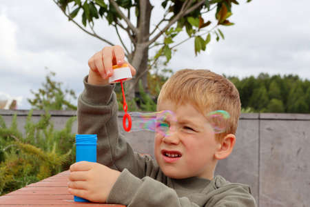 The blond boy squinted his eyes and makes soap bubbles. Five year old boy in soap bubbles.の写真素材