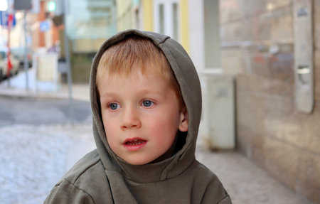 A blond boy in a hood looks dreamily into the distance. Thoughtful five year old boy.