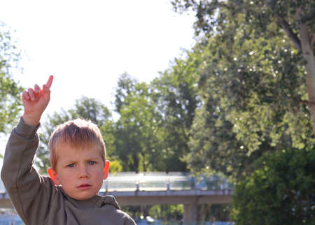 The blond boy furrowed his brows and raised his hand. Displeased five-year-old boy in the rays of sunlight.の写真素材
