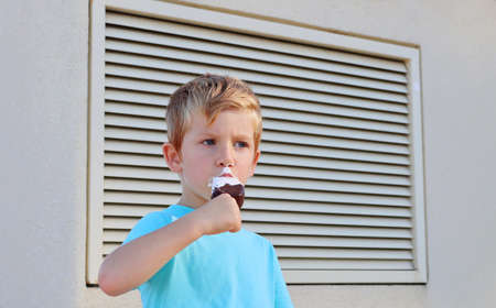 The blond boy eats ice cream and looks seriously into the distance. A thoughtful five-year-old boy.の写真素材